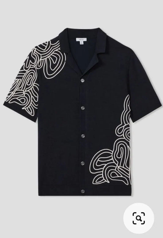 Close-up of white contour-line embroidery on shoulder of black camp shirt